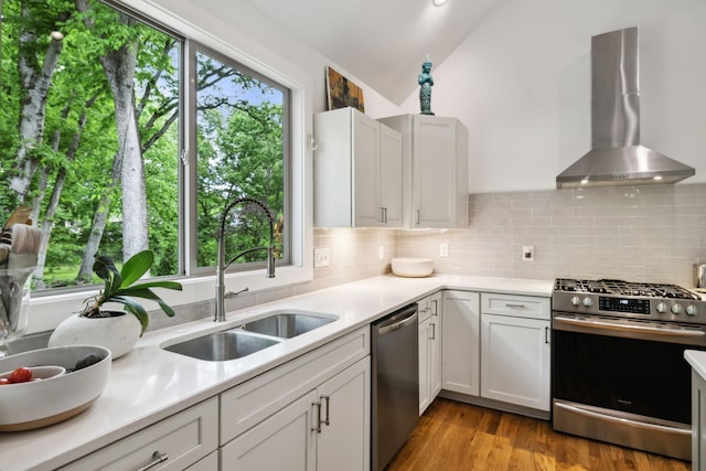 kitchen with a sink, wall chimney exhaust hood, stainless steel appliances, vaulted ceiling, and tasteful backsplash