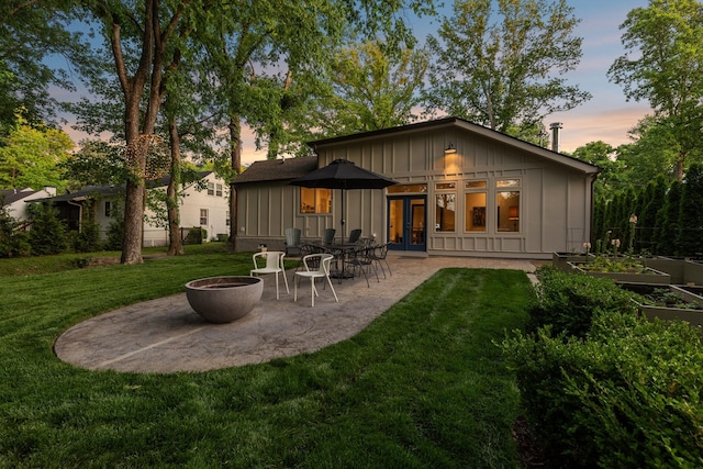 rear view of house featuring a fire pit, a yard, a patio, board and batten siding, and a vegetable garden