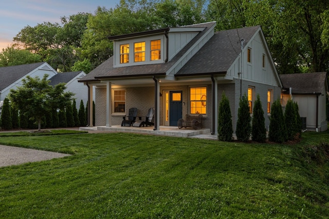 back of property at dusk featuring a yard, board and batten siding, brick siding, and a shingled roof