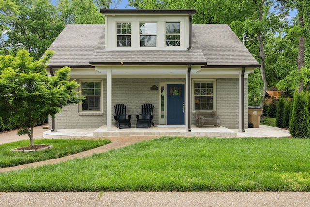 view of front of property with a front yard, roof with shingles, and brick siding