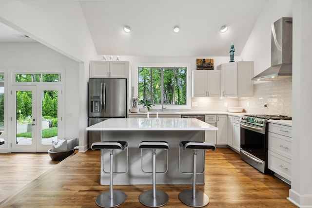 kitchen featuring appliances with stainless steel finishes, vaulted ceiling, a breakfast bar area, and wall chimney exhaust hood