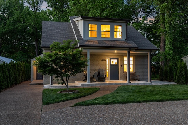 view of front of house with covered porch, brick siding, and a yard