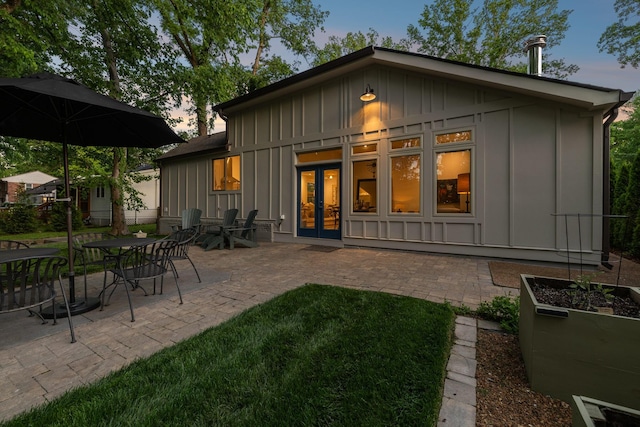 back of property at dusk with board and batten siding, a patio area, and french doors