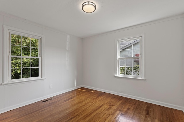 empty room with baseboards, a healthy amount of sunlight, visible vents, and wood finished floors