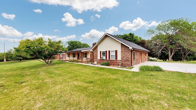 view of side of property featuring concrete driveway, brick siding, covered porch, and a lawn