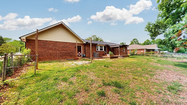 rear view of house with a lawn, central AC, brick siding, and fence