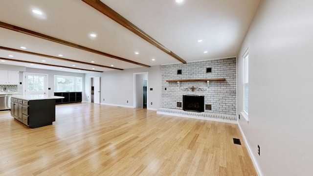 unfurnished living room featuring beam ceiling, visible vents, a fireplace, and light wood-style floors