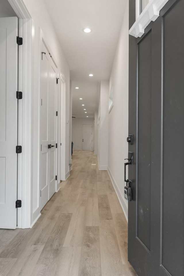 corridor with baseboards, light wood finished floors, and recessed lighting