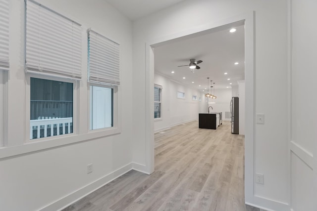 corridor featuring baseboards, light wood finished floors, recessed lighting, and a sink