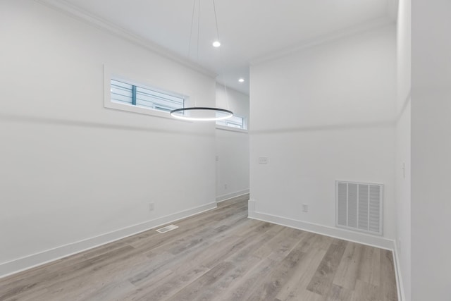 spare room featuring light wood finished floors, crown molding, visible vents, and baseboards