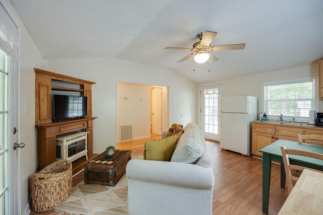 living area with a ceiling fan, a textured ceiling, light wood finished floors, visible vents, and vaulted ceiling