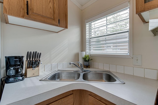 kitchen with brown cabinets, light countertops, crown molding, and a sink