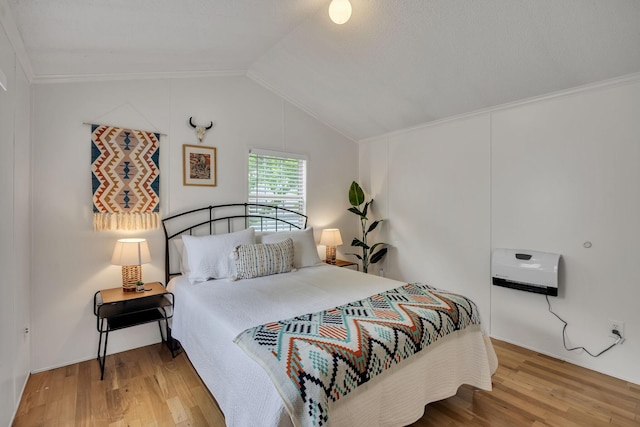 bedroom with vaulted ceiling, ornamental molding, heating unit, and wood finished floors