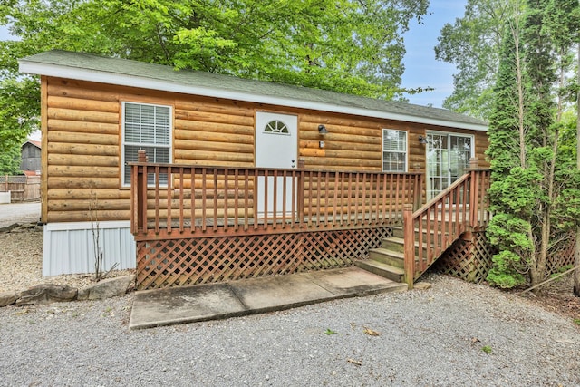 exterior space with a shingled roof, faux log siding, and a deck