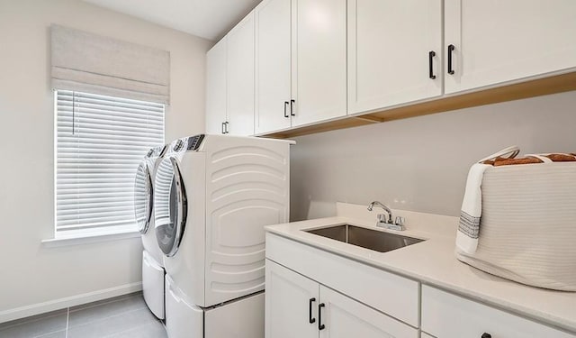 clothes washing area with baseboards, washer and clothes dryer, a sink, cabinet space, and light tile patterned floors