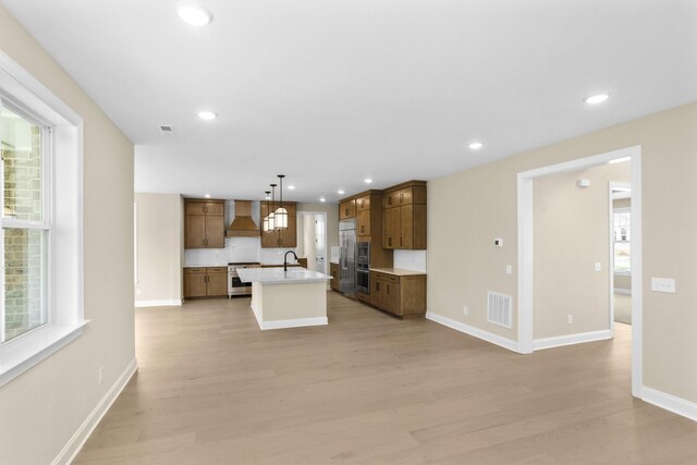 5958 Hunt Valley Dr, Spring Hill, TN 37174 - kitchen with wall chimney range hood, stainless steel appliances, light wood-type flooring, a center island with sink, and recessed lighting