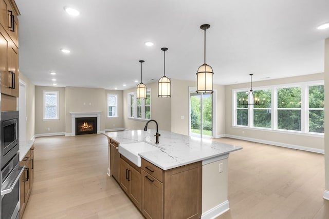 5958 Hunt Valley Dr, Spring Hill, TN 37174 - kitchen with a lit fireplace, open floor plan, light wood-style floors, brown cabinetry, and a kitchen island with sink