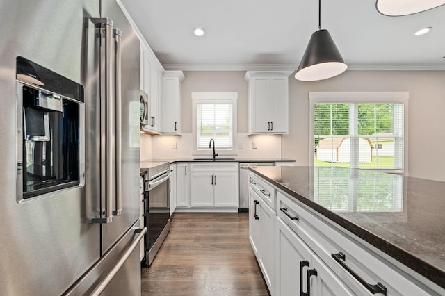 kitchen featuring a sink, stainless steel appliances, dark wood-style flooring, white cabinetry, and hanging light fixtures