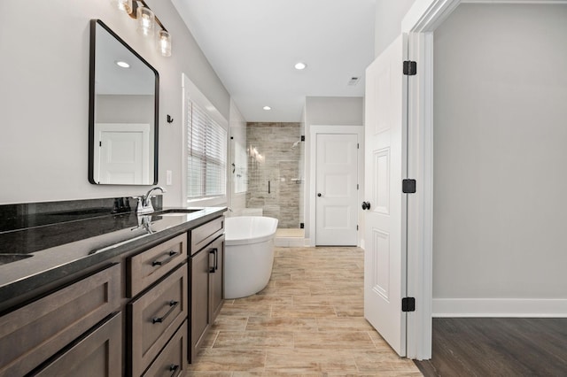 bathroom with a stall shower, vanity, a soaking tub, and wood finished floors