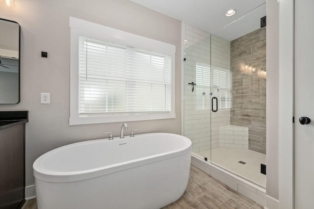 bathroom with a stall shower, recessed lighting, a soaking tub, vanity, and wood finished floors