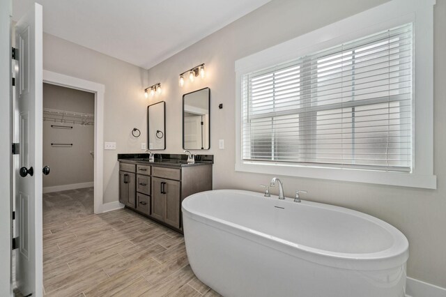 full bathroom featuring double vanity, wood finished floors, a walk in closet, baseboards, and a freestanding tub