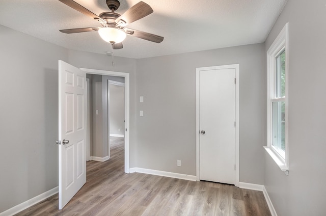 unfurnished bedroom featuring light wood-style flooring, a textured ceiling, baseboards, and a ceiling fan