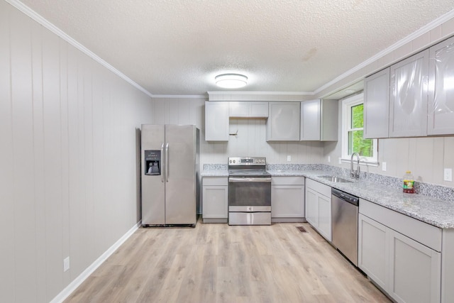 kitchen featuring a sink, a textured ceiling, light wood finished floors, crown molding, and appliances with stainless steel finishes