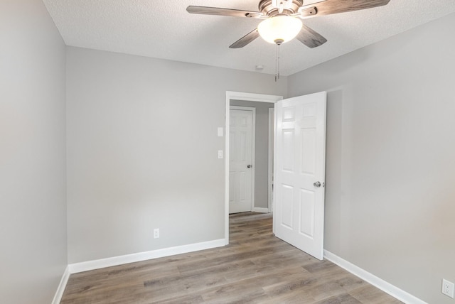 empty room featuring light wood-style flooring, a textured ceiling, baseboards, and a ceiling fan