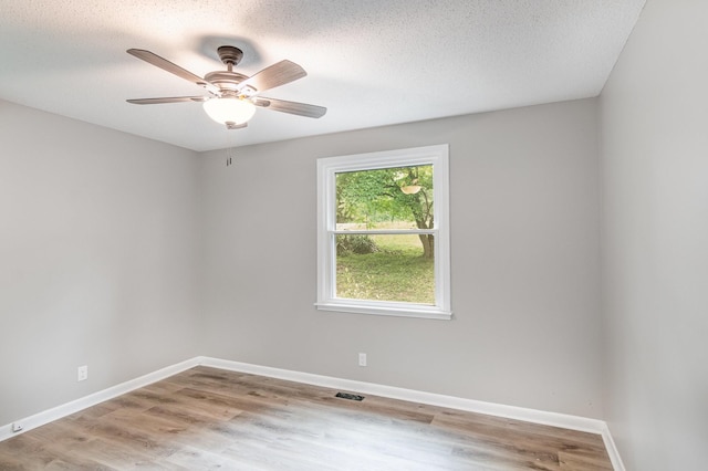 spare room with wood finished floors, a textured ceiling, visible vents, a ceiling fan, and baseboards