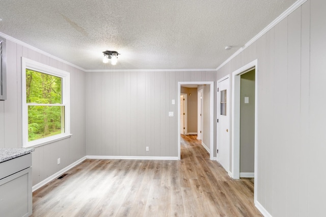 unfurnished room with a textured ceiling, visible vents, crown molding, light wood-style flooring, and baseboards