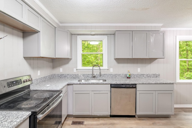 kitchen featuring a textured ceiling, ornamental molding, a sink, light wood-style floors, and appliances with stainless steel finishes