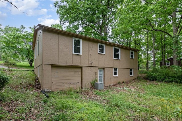 rear view of house with central air condition unit, a garage, and stucco siding