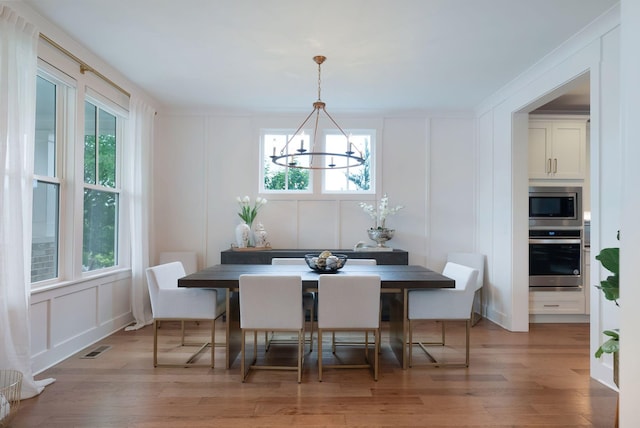 dining space with an inviting chandelier, a decorative wall, and light wood-type flooring