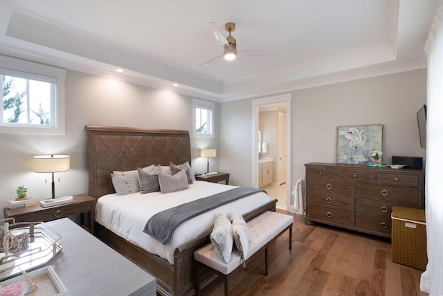 bedroom featuring light wood finished floors, a tray ceiling, ceiling fan, ensuite bath, and recessed lighting