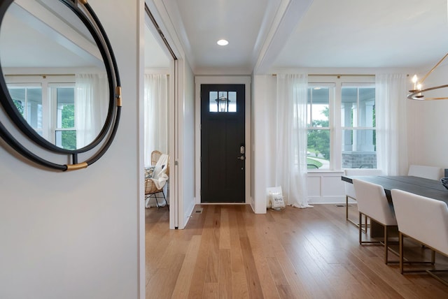 foyer entrance featuring an inviting chandelier, light wood-style floors, plenty of natural light, and beam ceiling