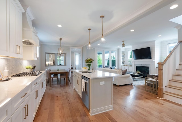 kitchen with light countertops, ornamental molding, light wood-style floors, stainless steel appliances, and a fireplace