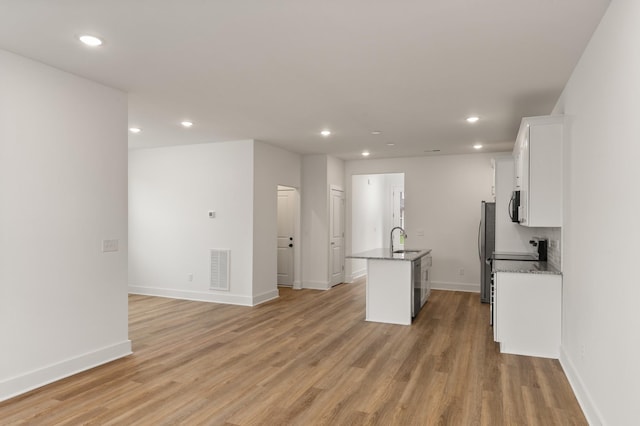 kitchen featuring freestanding refrigerator, recessed lighting, a kitchen island with sink, and white cabinets