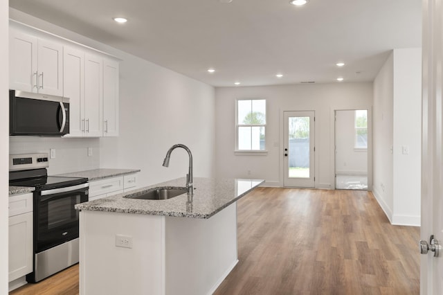kitchen featuring a sink, stainless steel appliances, light wood finished floors, backsplash, and white cabinetry