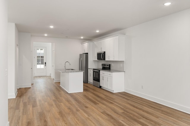 kitchen with light wood-style flooring, a sink, a center island with sink, white cabinetry, and appliances with stainless steel finishes