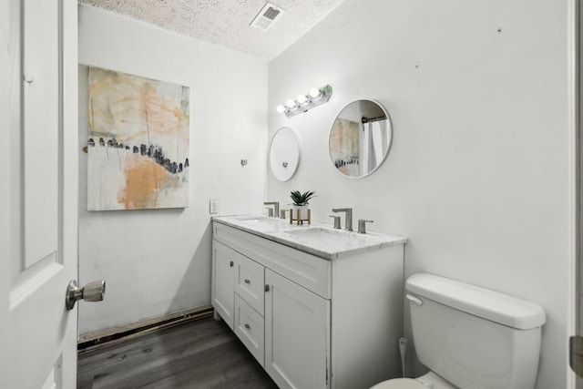 full bath featuring a sink, toilet, wood finished floors, a textured ceiling, and visible vents
