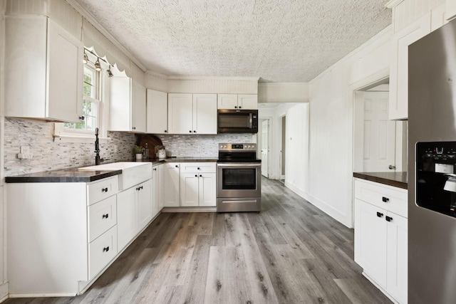 kitchen with light wood-style flooring, a sink, dark countertops, stainless steel appliances, and crown molding
