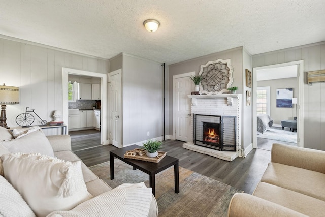 living room featuring baseboards, a brick fireplace, dark wood finished floors, and a textured ceiling