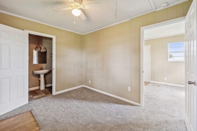 unfurnished room with a textured ceiling, attic access, carpet, crown molding, and a ceiling fan