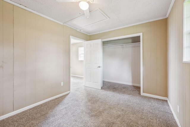 unfurnished bedroom featuring a textured ceiling, ornamental molding, attic access, and carpet