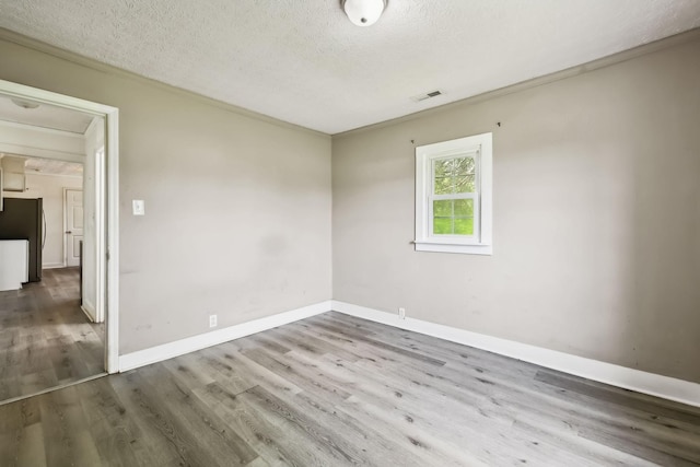 unfurnished room featuring wood finished floors, a textured ceiling, visible vents, crown molding, and baseboards