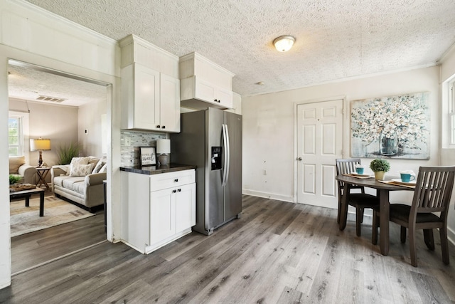 kitchen featuring wood finished floors, dark countertops, stainless steel refrigerator with ice dispenser, white cabinets, and visible vents
