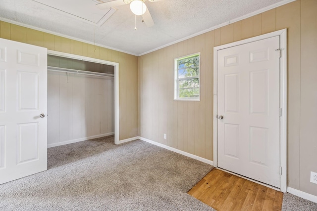 unfurnished bedroom featuring a closet, attic access, carpet, baseboards, and ornamental molding