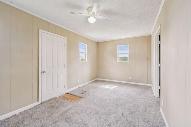 unfurnished bedroom featuring a textured ceiling, carpet, crown molding, a ceiling fan, and baseboards