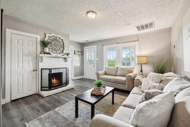living room featuring a textured ceiling, a brick fireplace, visible vents, and wood finished floors