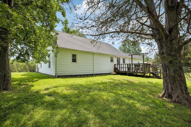 rear view of property featuring a lawn, a deck, and roof with shingles